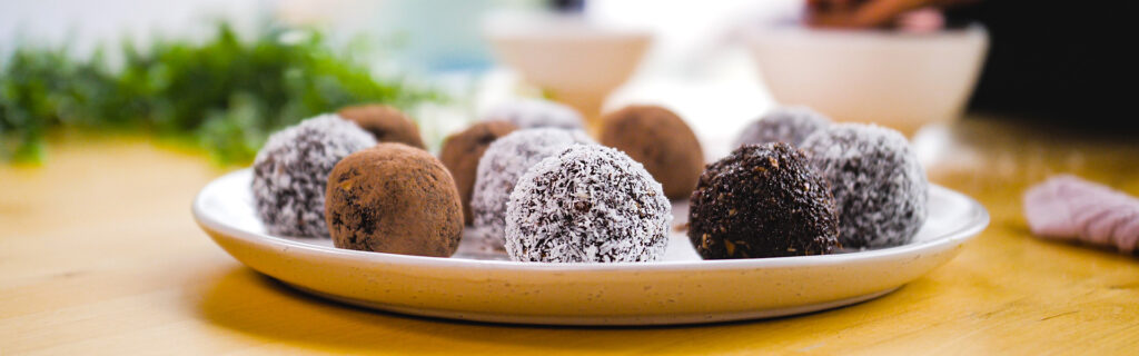 A variety of chocolate truffles, some covered with coconut and some dipped in cocoa, are arranged on a plate ready to eat